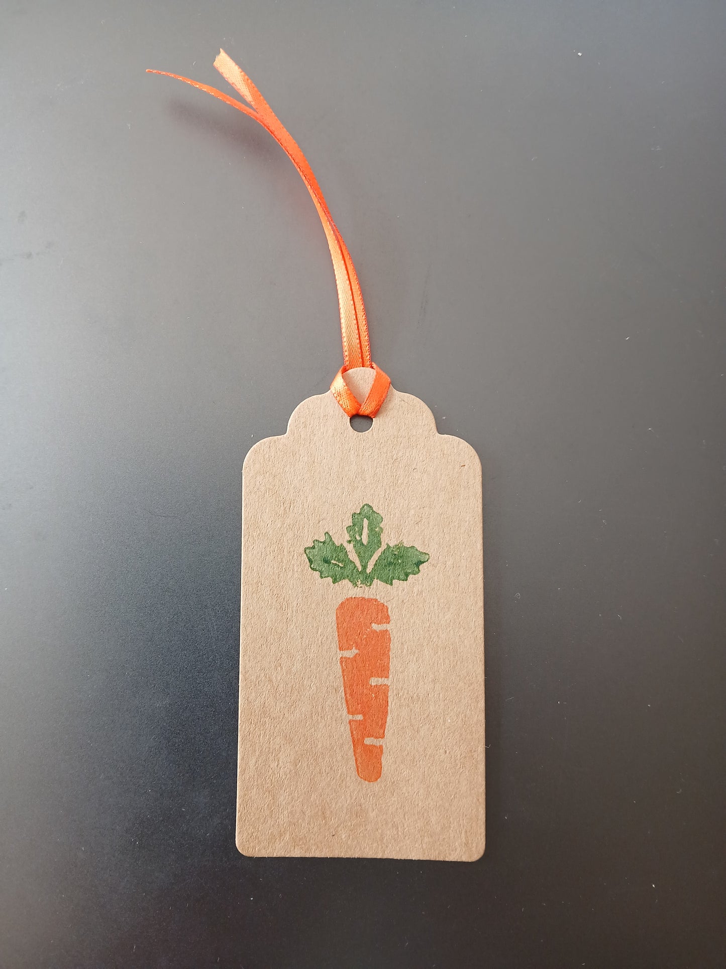 Carrot in Orange & Green on oblong brown gift tag with ribbon