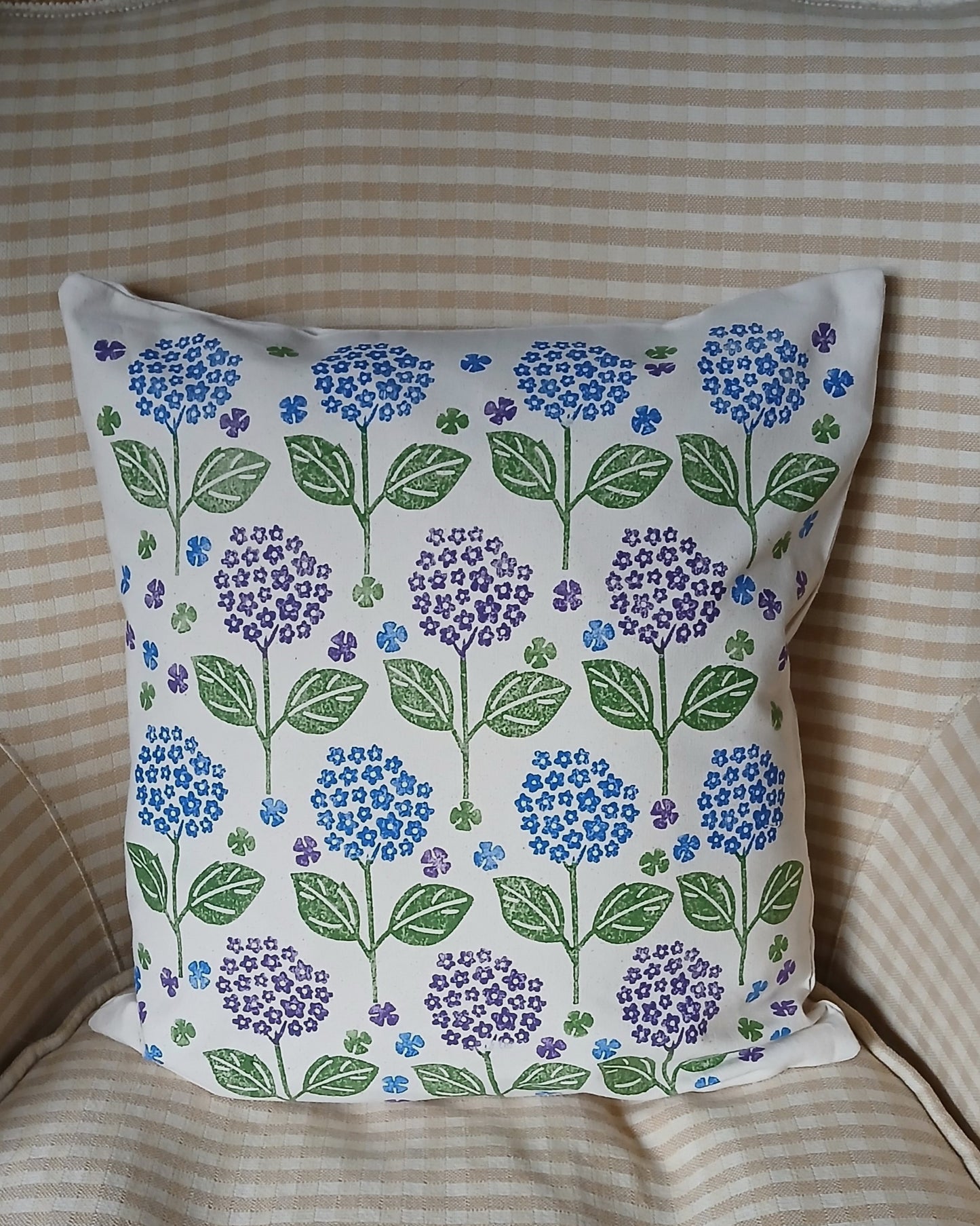 A square throw pillow with a white background and a repeating pattern of blue, purple, and green hydrangea flowers